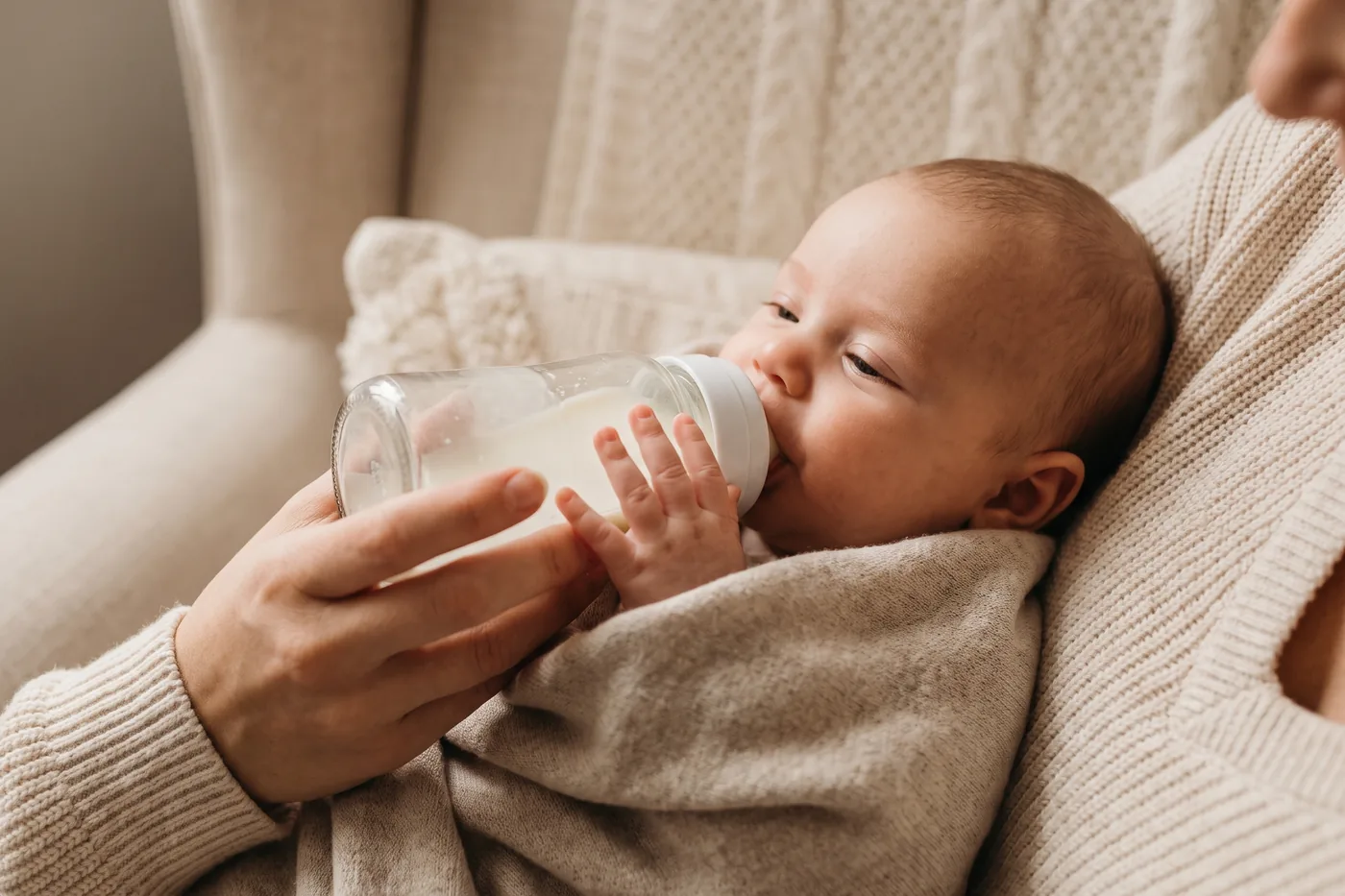 A baby bottle feeding, one hand resting on the bottle